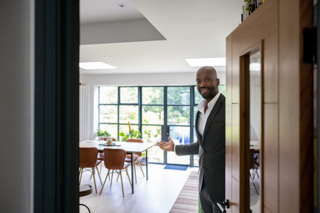 Welcoming black, male leader opening the door, looking at camera and smiling.